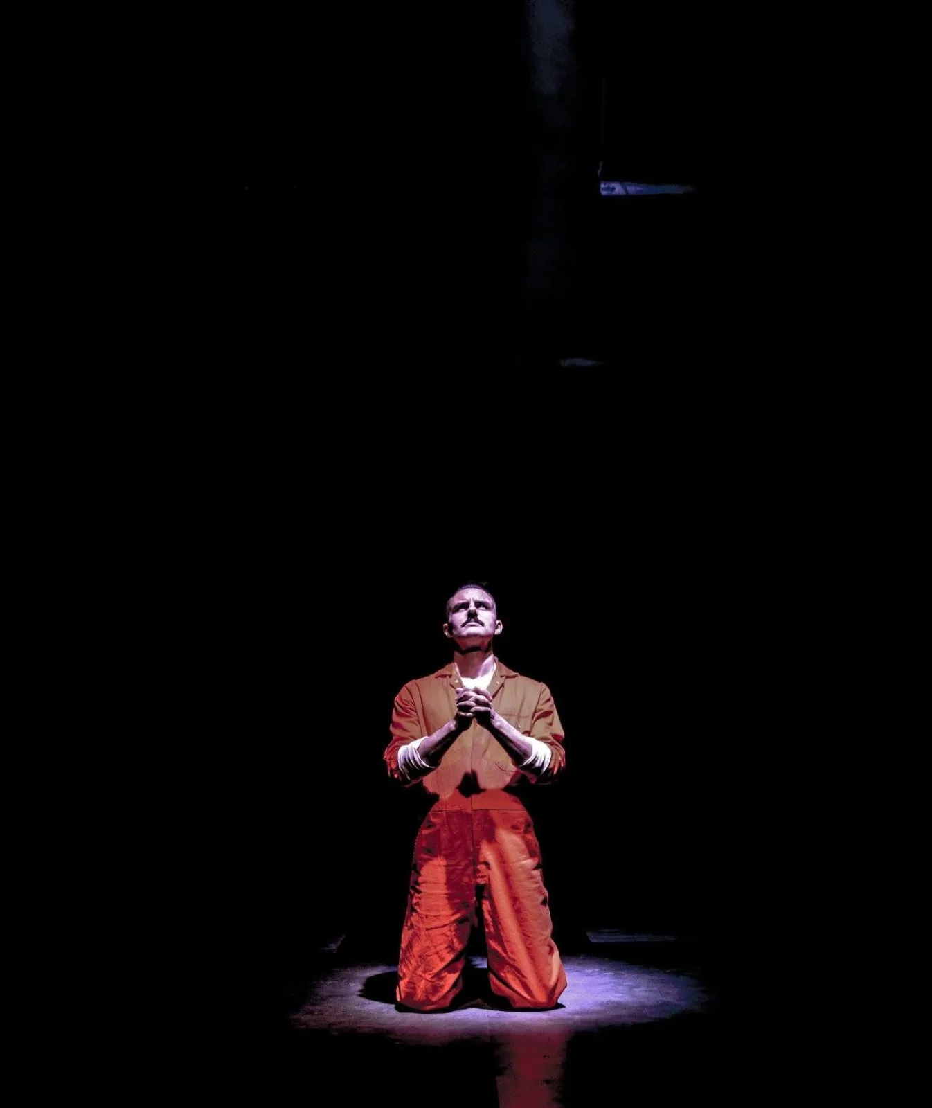 Danny Solomon on stage — orange jumpsuit kneeling, spotlit