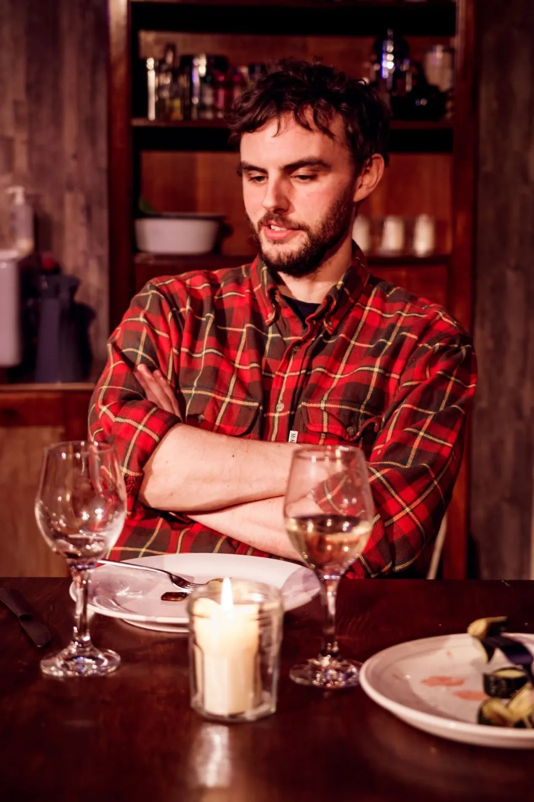 Danny Solomon on stage — plaid shirt, dinner table, arms crossed