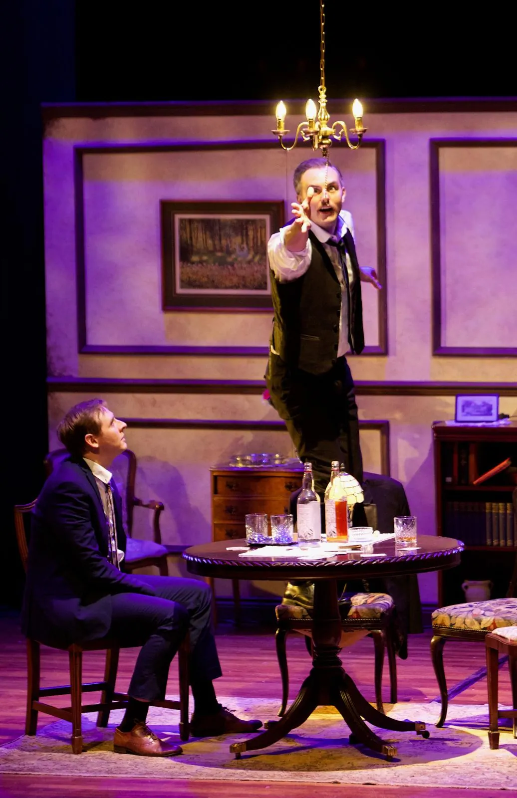 Danny Solomon on stage — standing on a table, reaching for a chandelier
