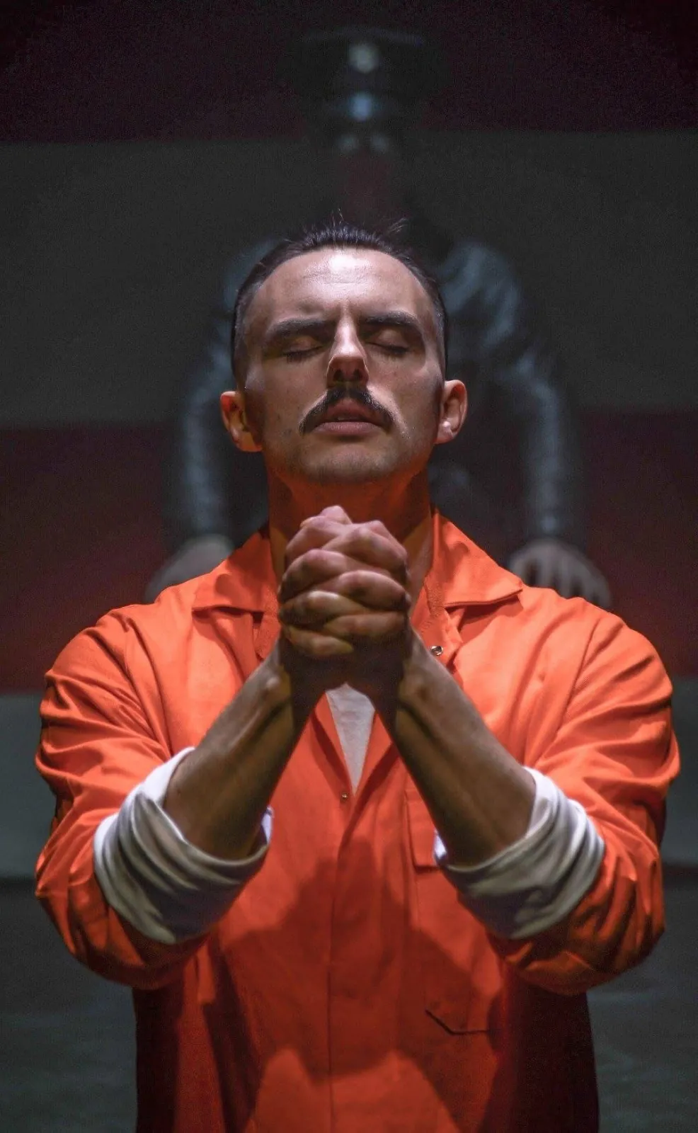 Danny Solomon on stage — orange jumpsuit, hands clasped, praying