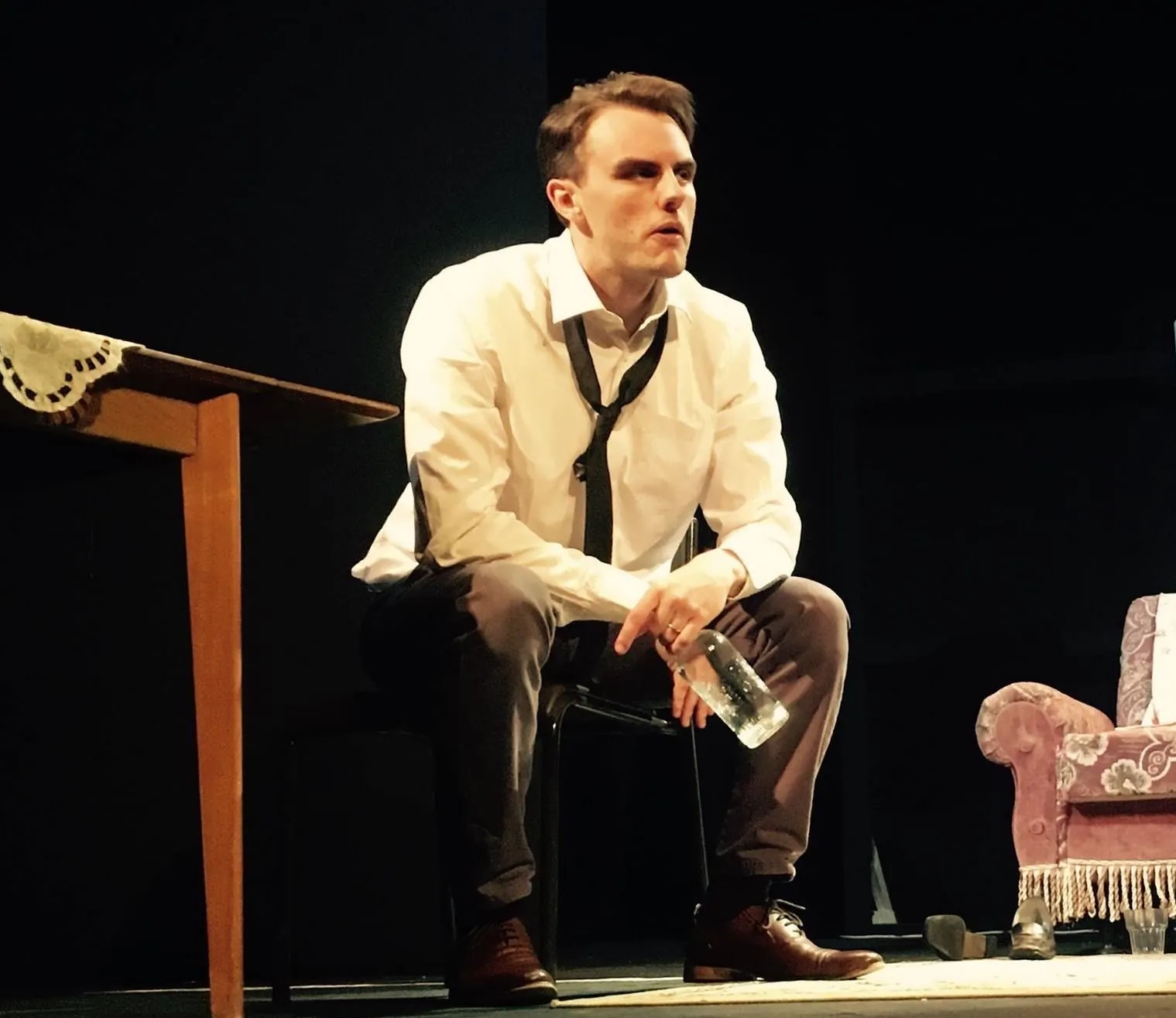 Danny Solomon on stage — seated, loose tie, holding a bottle