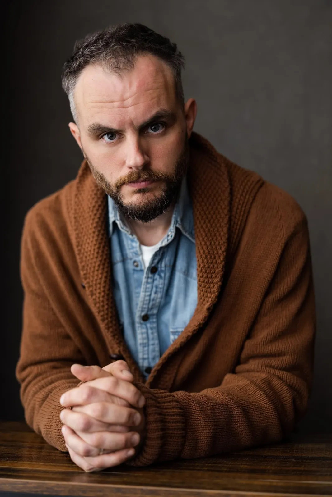 Danny Solomon portrait — brown cardigan, hands clasped